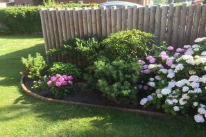 Ein Garten mit Holzzaun, verschiedenen Sträuchern und Hortensienblüten.