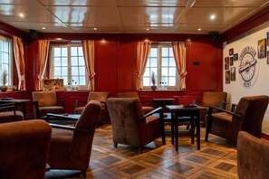 A room with red walls, wooden flooring, and multiple windows with curtains. There are several chairs and tables arranged for seating.