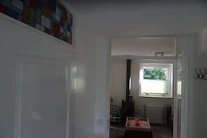 Ein Flur mit einer Tür, einem Heizkörper, einem Fenster und einem kleinen Tisch mit Gegenständen darauf.