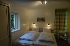 Ein Schlafzimmer mit einem Bett, zwei Nachttischlampen, einem Fenster, einem kleinen Tisch und einem Poster an der Wand.