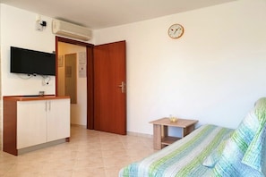 A room with a bed, a TV mounted on the wall, a wooden door, and a small table with a lamp. - Apartments Hošnjak (3) (Njivice)