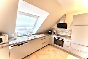 A modern kitchen with a built-in oven, a microwave, a coffee maker, and a window with blinds. - Holiday apartment with 2 bedrooms (Borkum)
