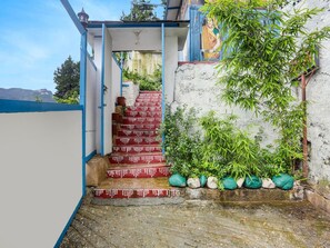 A staircase leading to a covered area with a mural, surrounded by greenery and a concrete wall. - Deluxe Palette Bhatta Falls (Dehradun)