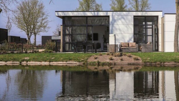 A modern house with a large glass window, a patio with outdoor furniture, and a pond in the foreground. - Holiday Home in Olburgen With Terrace (Olburgen)