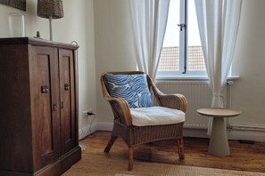 Ein Zimmer mit einem Korbstuhl, einem kleinen runden Tisch und einem dunklen Holzschrank.
