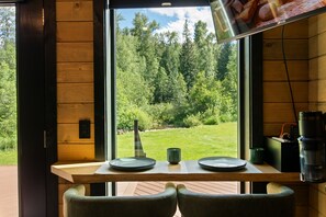 Una mesa de comedor con platos y una vela, una ventana con vista al bosque y una pared de madera.