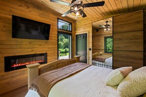 Ein Schlafzimmer einer Holzhütte mit Kamin, einem Bett, einem Deckenventilator und einem an der Wand montierten Fernseher.