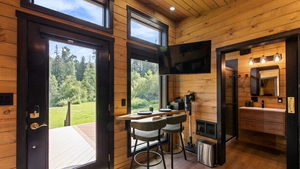 Houten hut interieur met een eethoek, keuken en een groot raam met uitzicht op het bos.