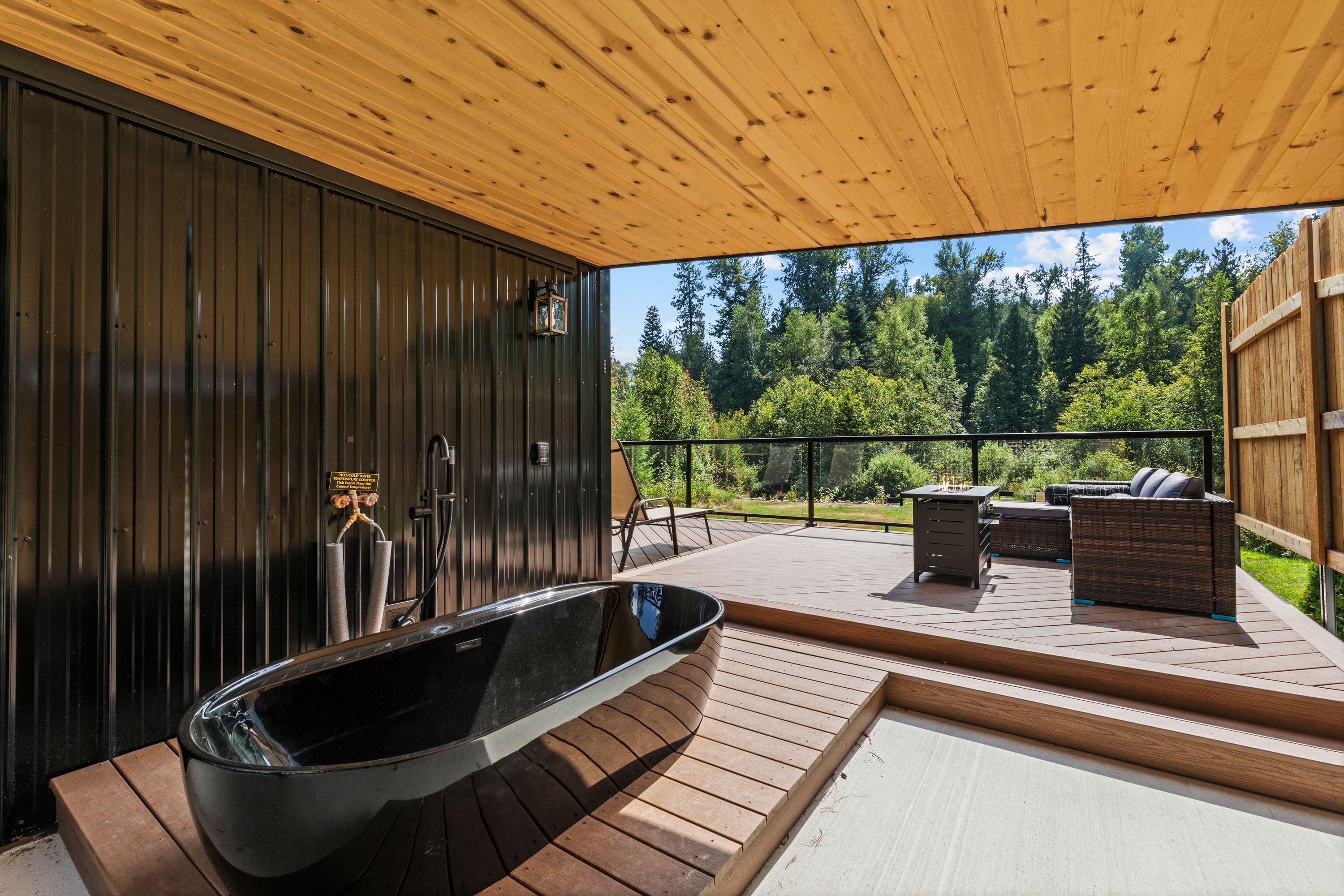 A modern outdoor hot tub area with a wooden deck, a built-in bench, and a view of a forested landscape.