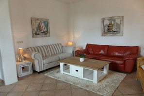 Ein Wohnzimmer mit einem gestreiften Sofa, einem roten Sofa, einem Holztisch und zwei Bildern an der Wand.