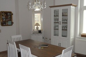 Ein Esszimmer mit Holztisch, weißen Stühlen, einer Chandelier und einer Vitrine mit Glastüren.