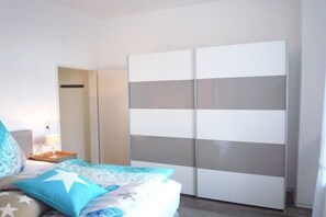 Ein Schlafzimmer mit Bett, Nachttisch, Kleiderschrank und einer Tür zu einem weiteren Raum.