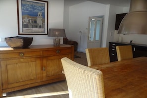 Ein Essbereich mit einem Holztisch, Korbstühlen, einem Holzschrank, einer Lampe und einem gerahmten Bild an der Wand.