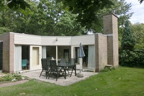 Ein überdachter Patio-Bereich mit Tisch und Stühlen, ein Ziegelkamin und eine Rasenfläche.