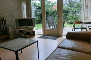 Ein Wohnzimmer mit Fernseher, einer Couch, einem Couchtisch und einer Glastür, die zu einer Außenpatio führt.