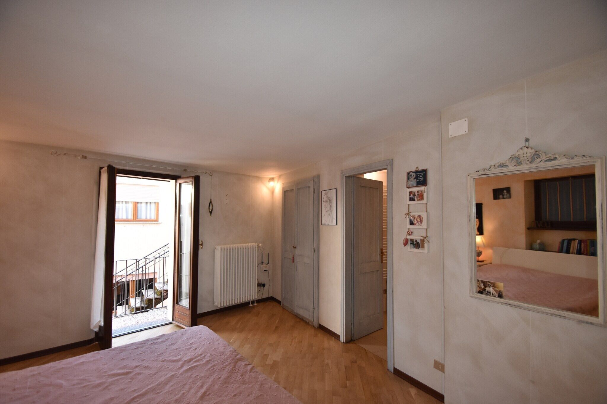 Une chambre à coucher comprenant un lit, un radiateur, une porte donnant sur un balcon et un miroir orné de tableaux.