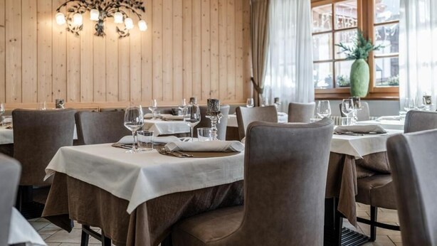Restaurant amb parets de fusta, taules cobertes amb estores blanques i caires.