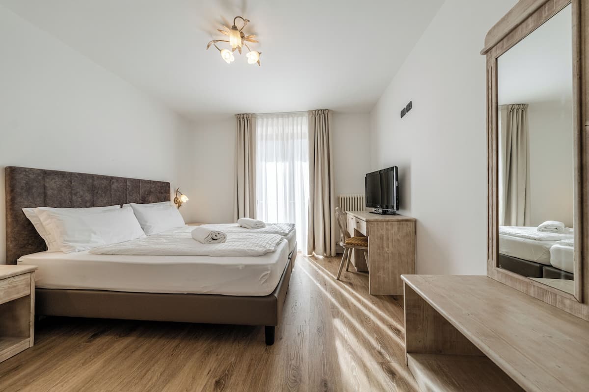 Una habitación de hotel con cama, escritorio, televisor y un espejo grande.