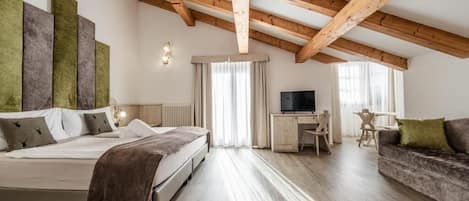 A bedroom with a bed, a desk, a television, and a sofa.