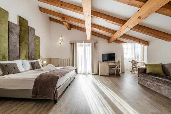 Quarto com cama, escrivaninha, televisão e sofá.