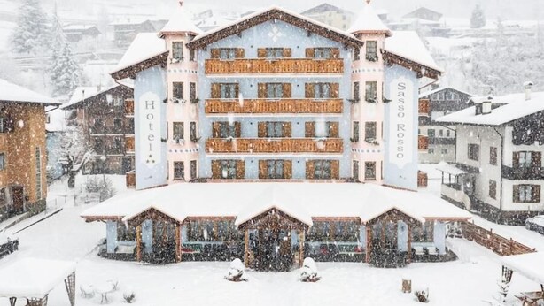 Un hotel de varios pisos con balcones, una entrada central y un paisaje nevado.