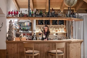 A bar area with wooden furniture, a Christmas tree, and various bottles on shelves. - HOTEL SASSO ROSSO (Mestriago)