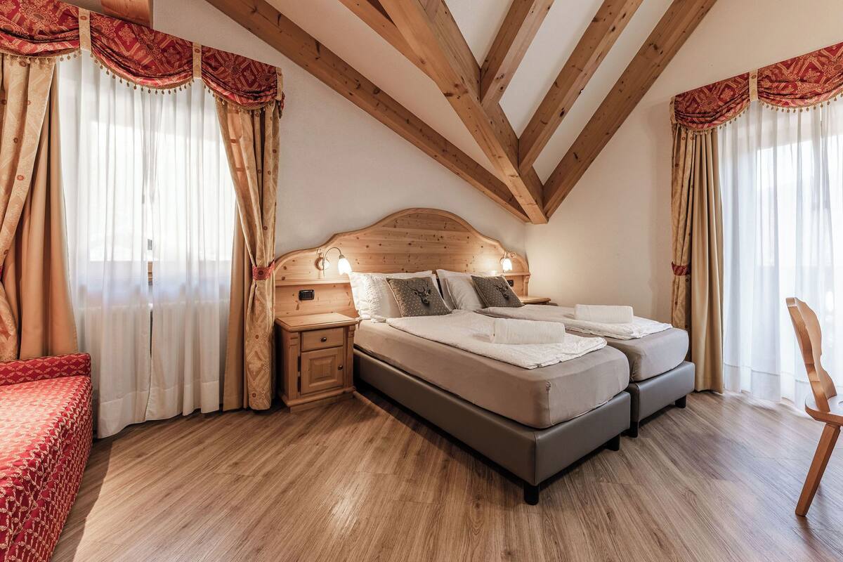Un dormitorio con techo de madera, una cama doble, lámparas de noche y cortinas.