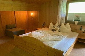 A wooden cabin room with a bed, a bench, a wall-mounted light, and a window with a plant. - Holiday apartment Vogelnest (Hippach)