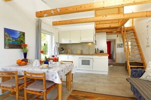 Eine gemütliche Küche mit Holzbalken, einem Essbereich mit Tisch für zwei Personen und einer Treppe zu einer oberen Ebene.