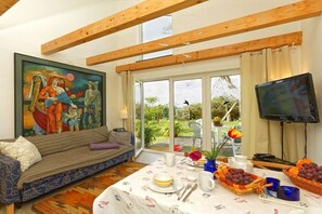 Ein Zimmer mit einer Couch, einem Esstisch mit Obst, einem Gemälde und einem Fernseher.