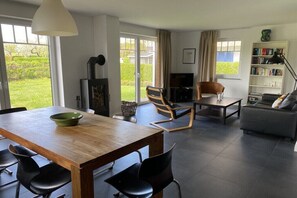 Ein modernes Wohnzimmer mit einem Holzesstisch, schwarzen Stühlen, einer Couch, einem Bücherregal und einem Kamin.