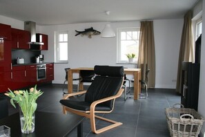 Eine moderne Küche mit roten Schränken, ein Essbereich mit einem schwarzen Stuhl und einer Fischdekoration an der Wand.