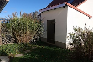 Ein kleines, weißes Gebäude mit rotem Dach, einer schwarzen Tür und einem Garten mit verschiedenen Pflanzen.