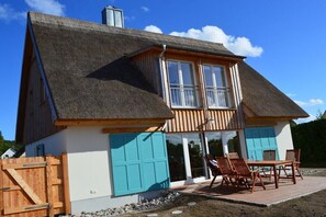 Ein zweistöckiges Haus mit einem Strohdach, einer Holzterrasse und einer Schiebetür.