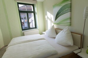 A room with two beds, a window with a view of buildings, and a green abstract painting on the wall. - Holiday home in Malchow with swimming pool (Malchow)