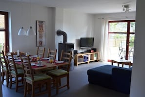 A dining area with a table set for four, a television on a stand, and a sofa in the living room. - Holiday home in Stolpe with swimming pool (Stolpe)