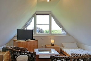 A small, cozy room with a television, a bedside table with a lamp, a bed, and wicker furniture. - Holiday apartment in Glowe with swimming pool (Glowe)