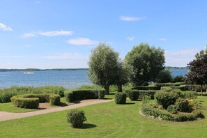 Ein angelegter Garten mit einem Weg, der zu einem Gewässer führt, umgeben von ordentlich geschnittenen Hecken und Bäumen.