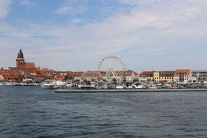 Ein Stadtbild am Wasser mit einem markanten Riesenrad, historischen Gebäuden und einem Yachthafen mit Booten.