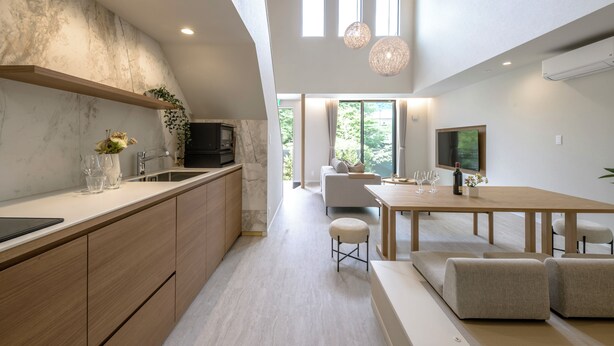 Een moderne keuken met een marmeren spatwand, houten keukenkastjes en een eethoek met een grote tafel en stoelen.