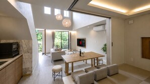 Een modern interieur met een eethoek, keuken en woonruimte, met een flatscreen-tv, hanglampen en grote ramen.