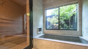 Een moderne badkamer met een houten vloer, een badkuip en een groot raam met uitzicht op bomen.