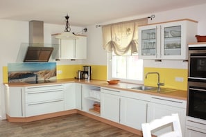 A kitchen with white cabinets, a wooden countertop, a sink, a stove, and a window with curtains. - Godewind on the Baltic Sea (Glowe)