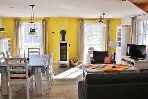 A living room with a dining area, a fireplace, a television, and a window with curtains. - Godewind on the Baltic Sea (Glowe)