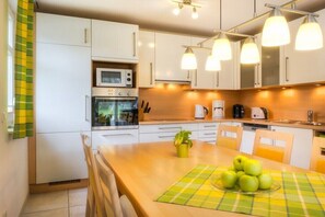 Eine moderne Küche mit weißen Schränken, einer Mikrowelle, einem Backofen und einem Essbereich mit Tisch für zwei Personen.