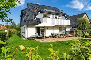 Ein zweigeschossiges Haus mit Balkon, einer Terrasse mit Gartenmöbeln und einem gepflegten Rasen.