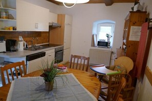 Eine kleine Küche mit weißen Schränken, einem Esstisch mit Stühlen und einem Fenster mit Blick.