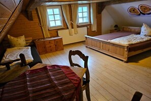 Ein gemütliches Schlafzimmer im Dachgeschoss mit Holzboden, einem Bett, einem Tisch mit Streifen-Tischdecke, einem Sessel und einer kleinen Kommode.