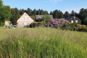 Ländliche Szenerie mit einem traditionellen Fachwerkhäuschen, einer Holzbude und einem Spielplatz.