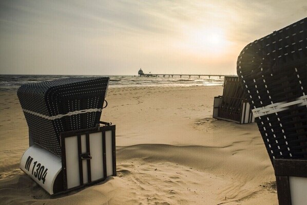 Strandkörbe an einem sandigen Strand, im Hintergrund ein Steg.